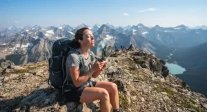 A tired hiker resting at a mountain summit and using a battery-operated portable fan for hiking.